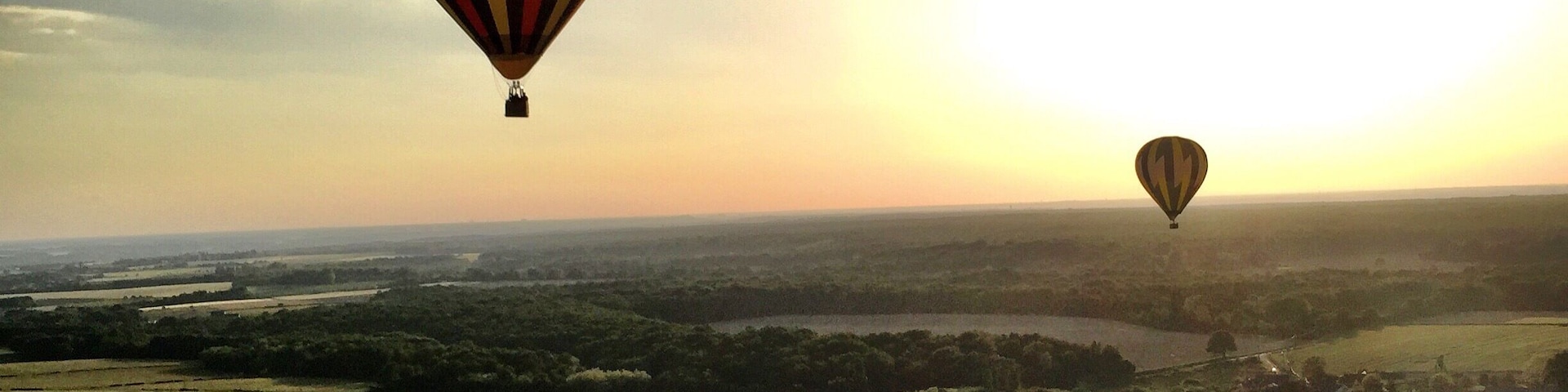 Two hot air balloons flying over a rural landscape with fields and a river.