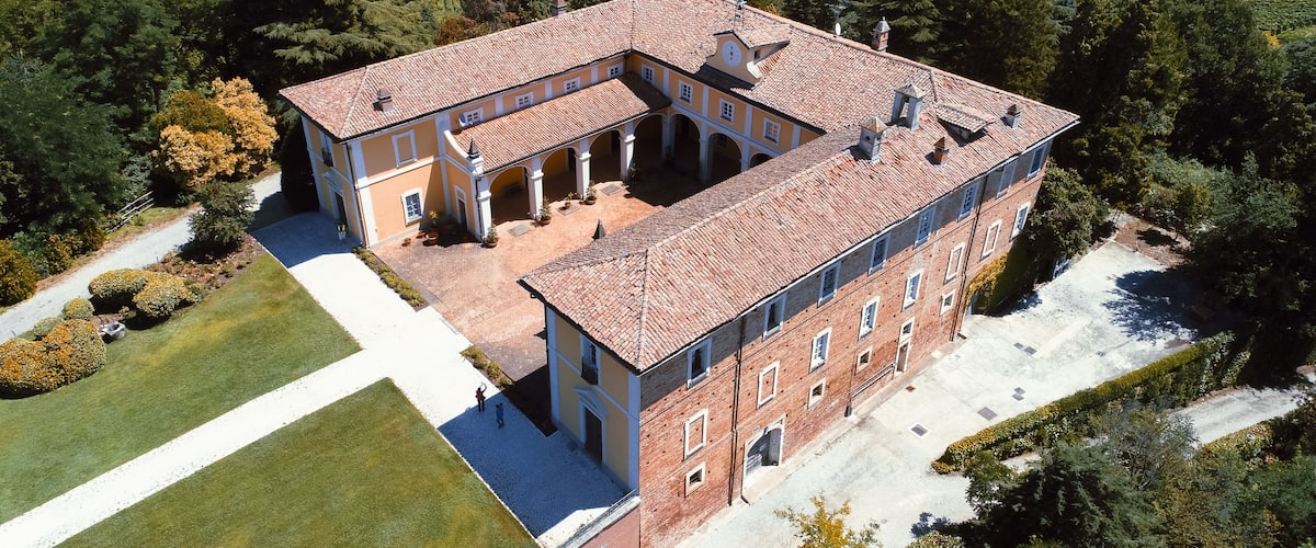 A large, historic building with a courtyard surrounded by lush vineyards.