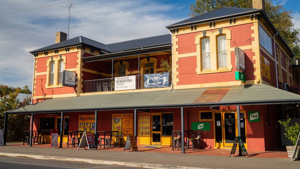 A two-story building with a red and yellow facade, a balcony, and various signs including one for a bottle shop.