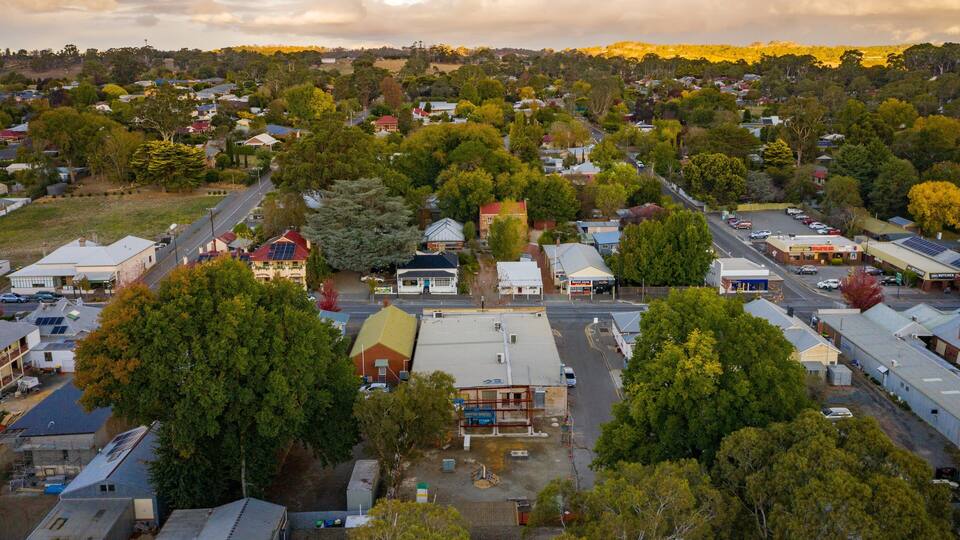 A town with a mix of residential and commercial buildings, surrounded by dense greenery and hills in the background.