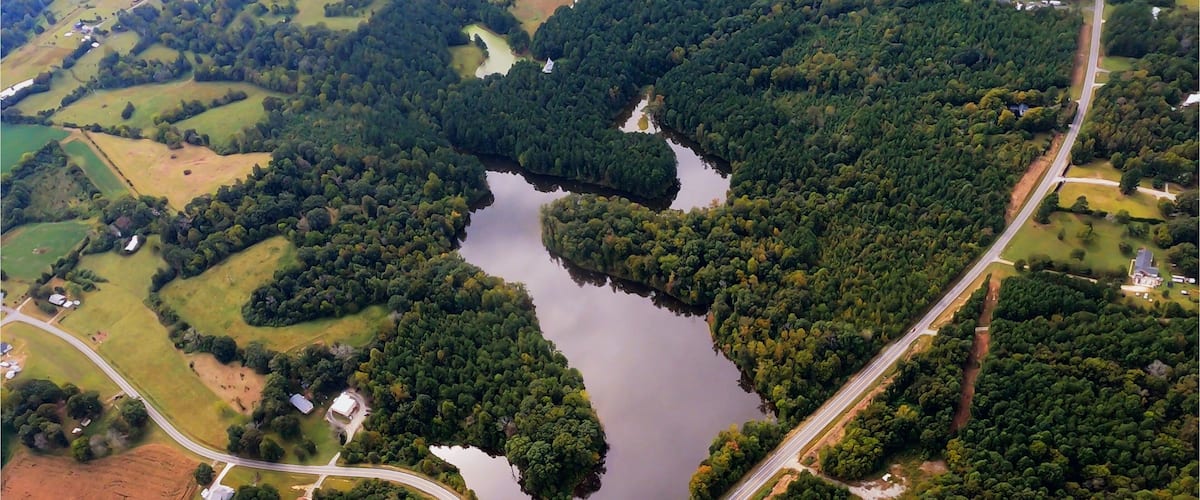 I fly over a very serene scene of a lake with a bridge, the sun glints off the lake and the clouds can be seen in the reflection off the lake. Very calming and a great peaceful shot. Randleman Lake in