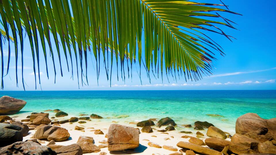 A beach with clear turquoise water, white sand, and large rocks.
