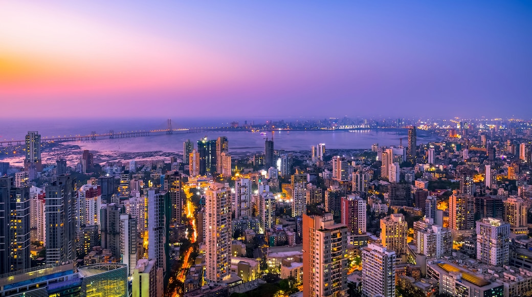A cityscape at dusk with illuminated buildings and a bridge in the distance.