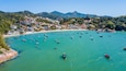 Une ville côtière où l’on peut admirer de nombreux bateaux sur des eaux turquoise, une plage de sable fin et, en arrière-plan, des collines et des montagnes verdoyantes.