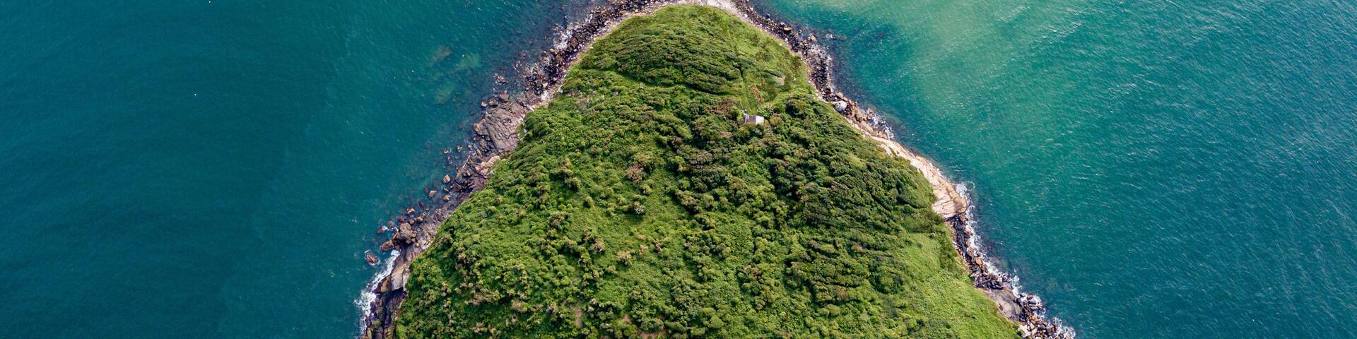 Aerial view of a triangular-shaped island in green sea (Batuta Island, Imbituba, Brazil)