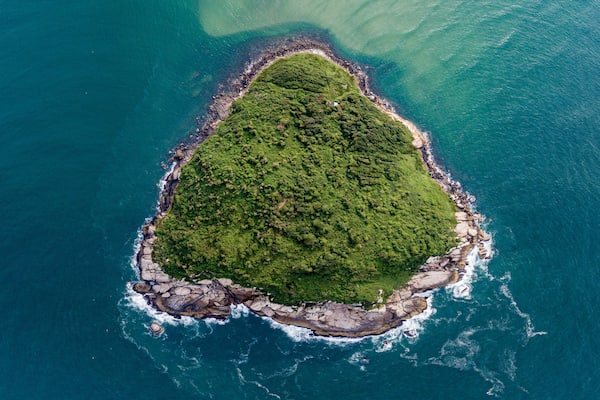 Aerial view of a triangular-shaped island in green sea (Batuta Island, Imbituba, Brazil)
