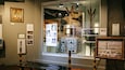 Une exposition présentant du matériel scientifique, des œuvres d’art encadrées et des panneaux d’information.