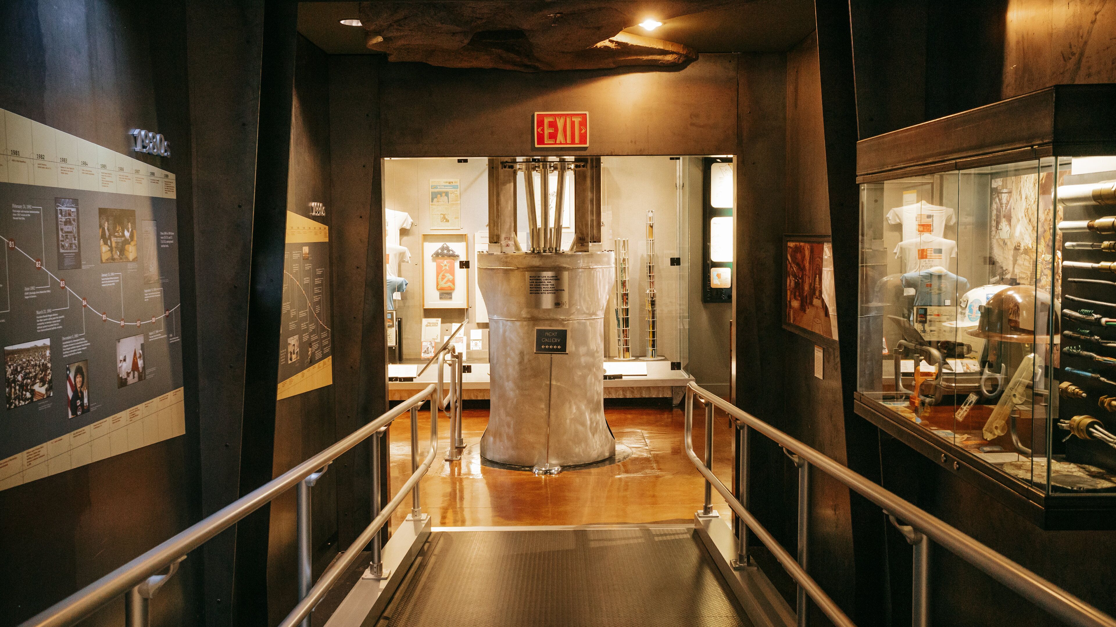 A museum corridor with an exit sign, a timeline on the left, and various exhibits on the right.