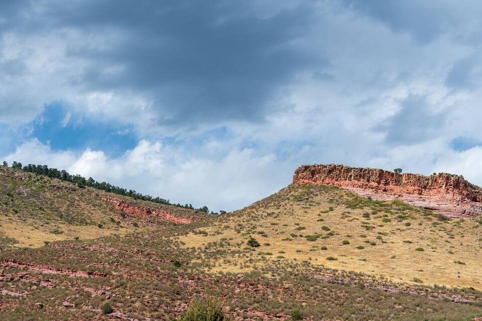 A rugged hill with sparse vegetation and a rocky outcrop under a cloudy sky.