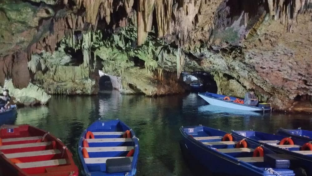 Une grotte ornée de stalactites, avec une rangée de bateaux amarrés à l’entrée.