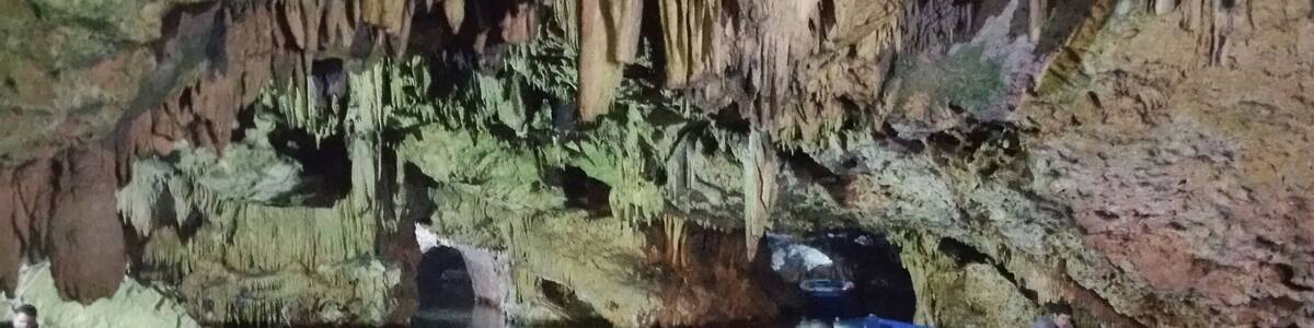 Eine Höhle mit Stalaktiten und eine Reihe von Booten, die am Eingang festgemacht sind.