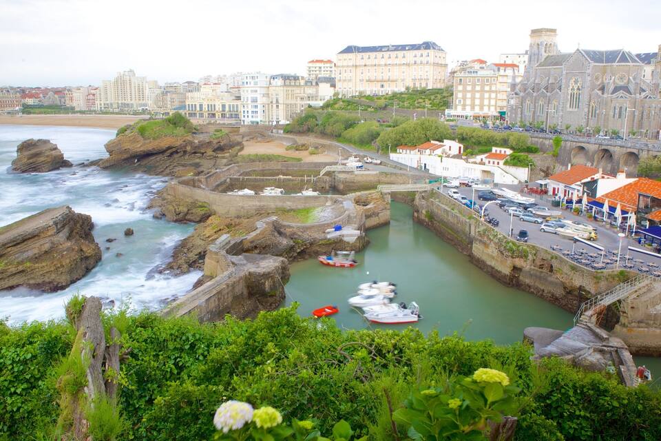 Un pueblo costero con costas rocosas, un puerto con barcos y edificios históricos.
