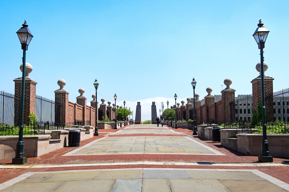 A paved pathway flanked by brick walls and street lamps.