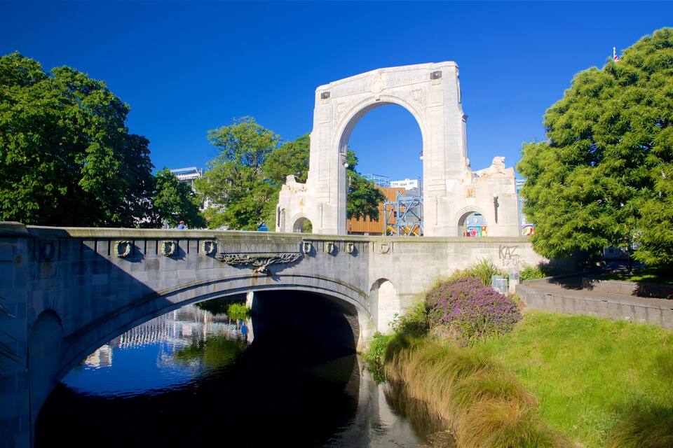 Uma ponte de pedra com arco sobre um canal, rodeada por árvores e vegetação.