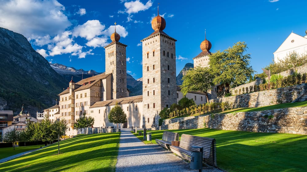 Ein historisches Gebäude mit Türmen und Kuppeln, umgeben von einer gepflegten Rasenfläche und einer Steinmauer.