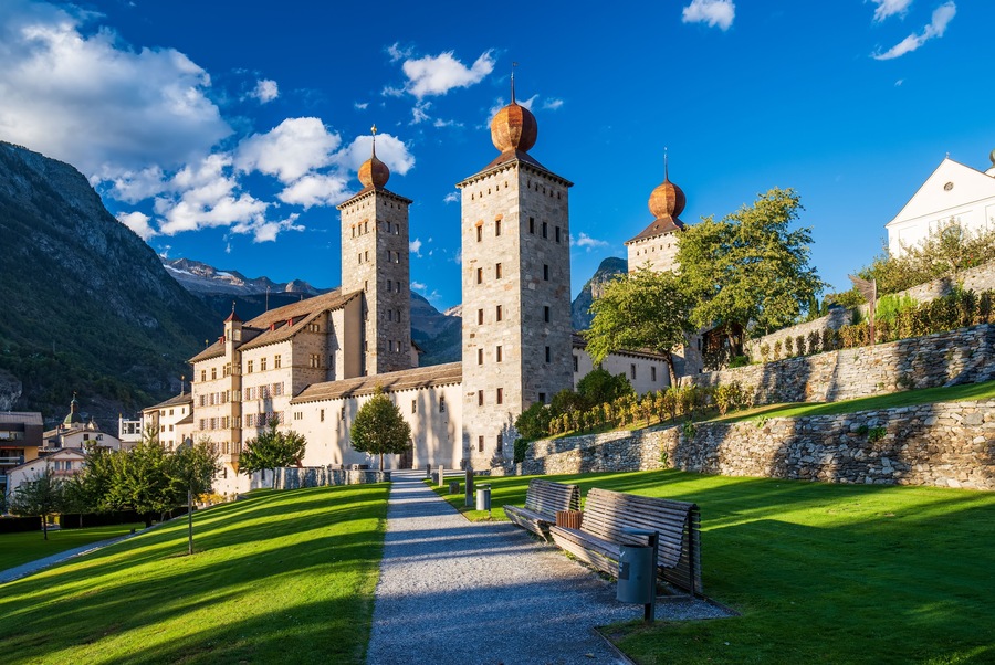 A historic building with towers and domes, surrounded by a well-maintained lawn and a stone wall.