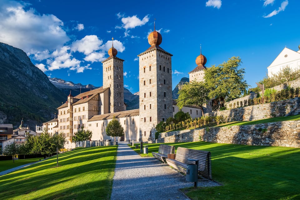 A historic building with towers and domes, surrounded by a well-maintained lawn and a stone wall.