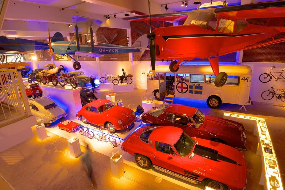A museum exhibit with vintage cars, motorcycles, bicycles, and a red airplane.