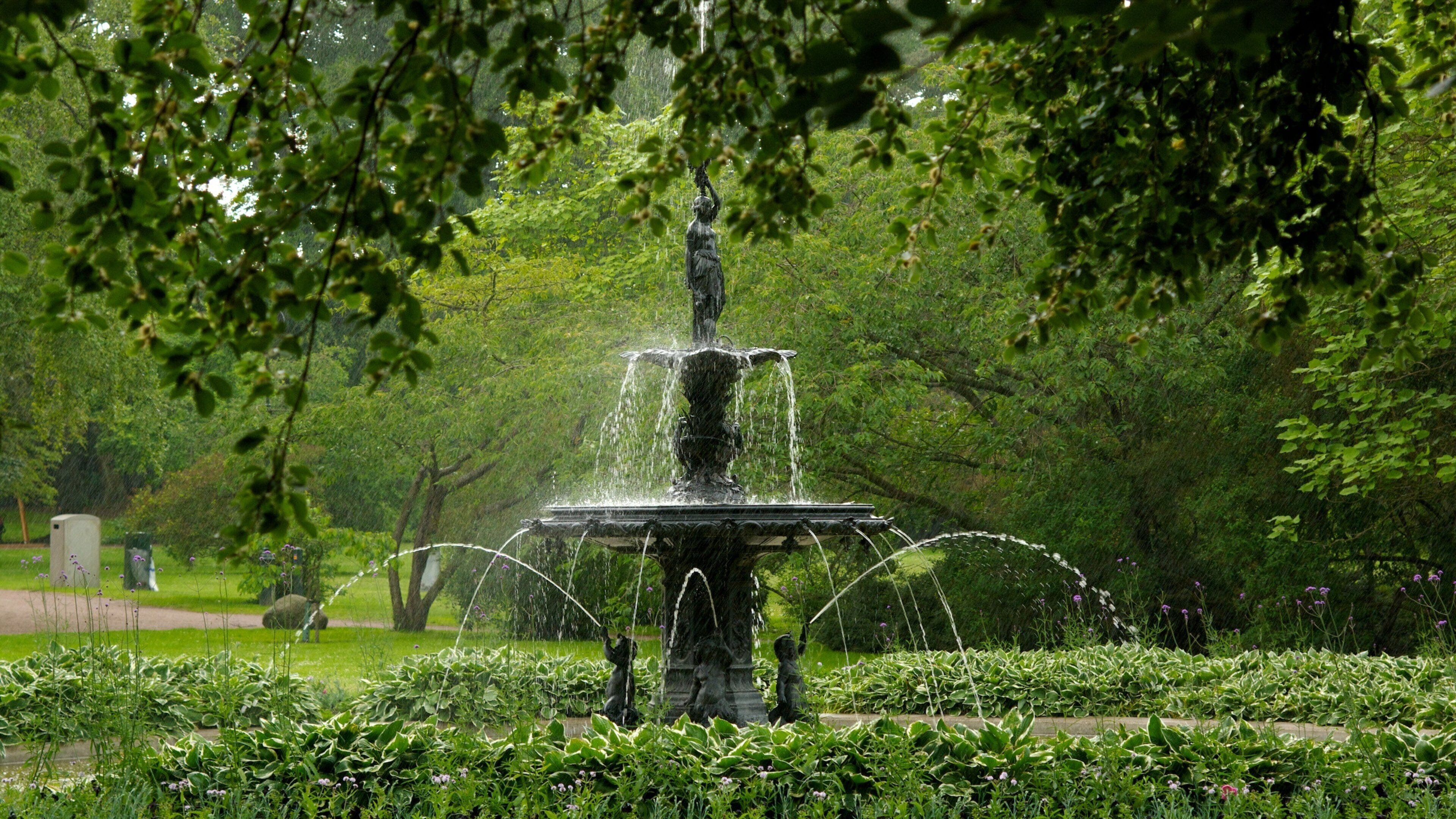 Une fontaine avec des jets d’eau, située dans un parc verdoyant et arboré.