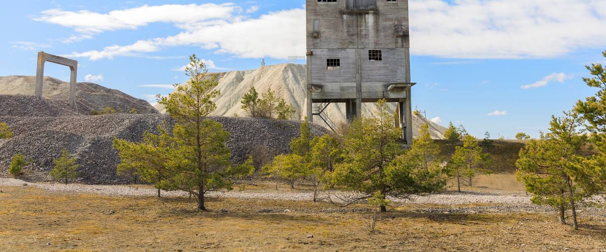 A concrete tower with a flag, surrounded by sparse trees and a rocky landscape.