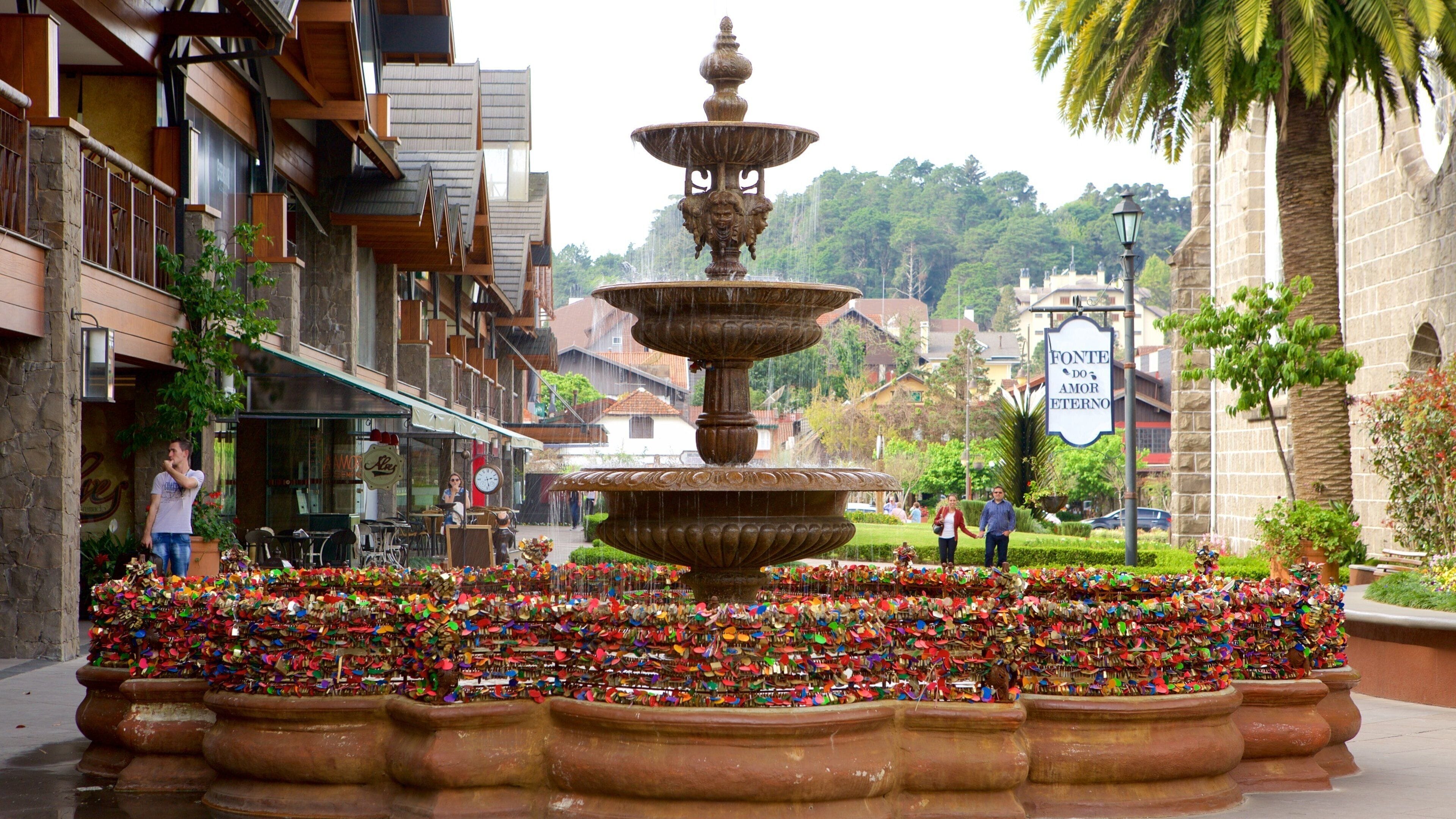A multi-tiered fountain with colorful locks in the foreground, surrounded by buildings and a sign reading "Fonte do Amor Eterno".