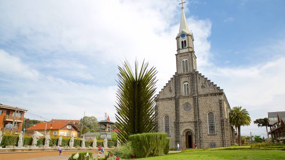 Une église dotée d’un clocher imposant et d’une horloge, entourée de statues et de verdure.