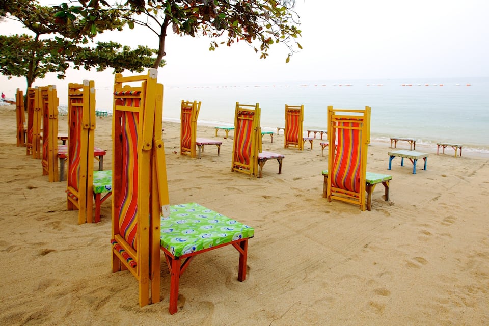 A beach with colorful beach chairs and tables, a sandy shore, and a calm sea.
