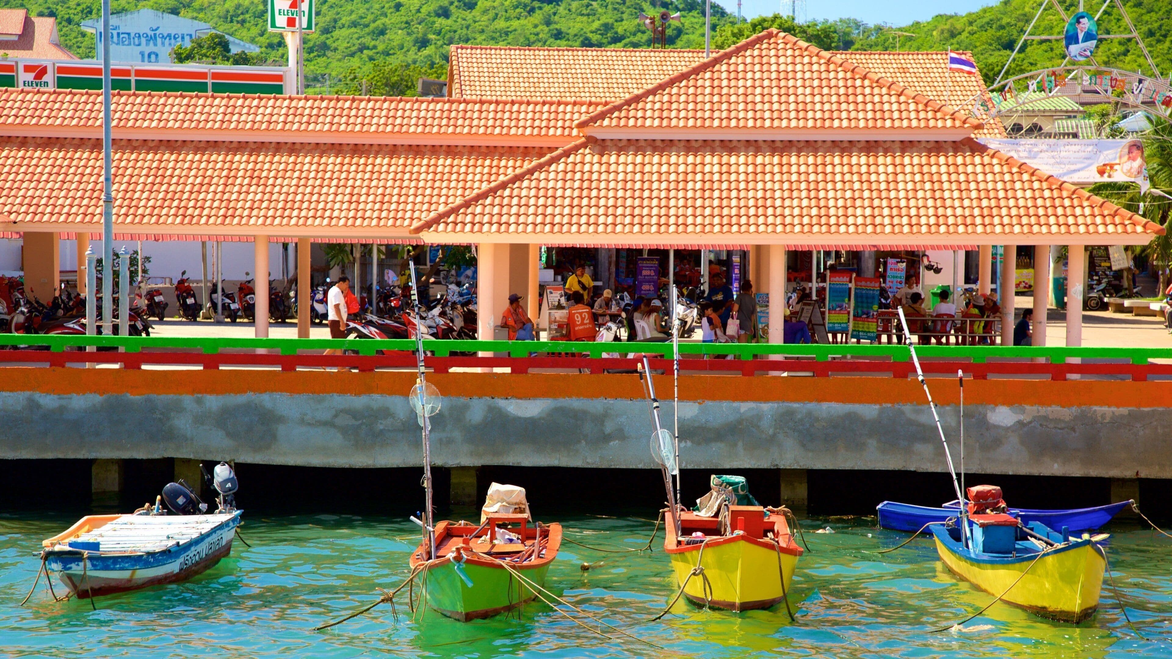 A coastal area with a traditional building, colorful boats, and a Seven Eleven convenience store.