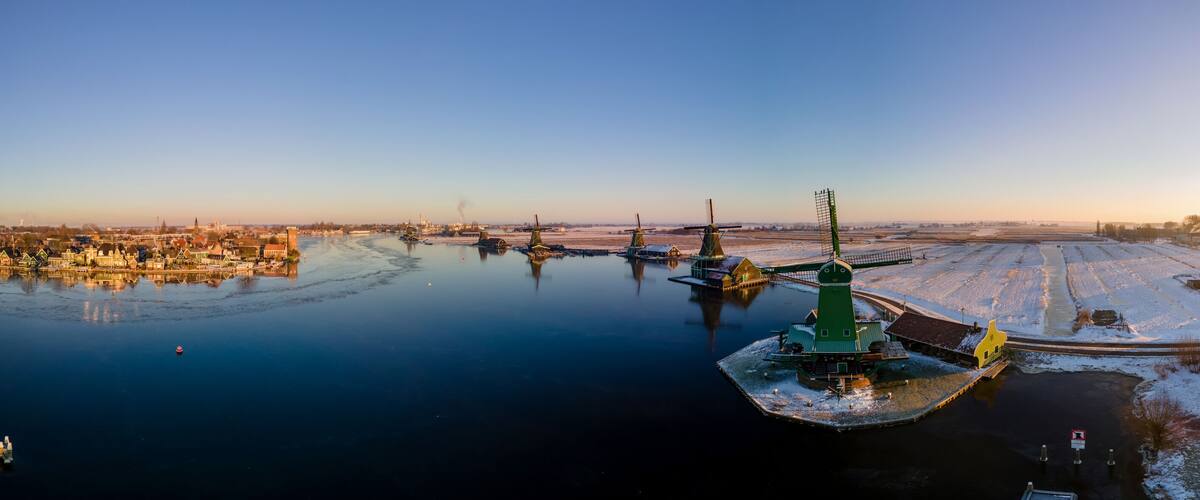 A frozen river with a green structure in the center, surrounded by snow-covered buildings and fields.