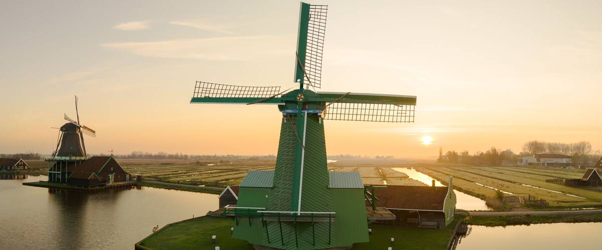 A green windmill on a small island surrounded by calm water, with a sunset in the background.