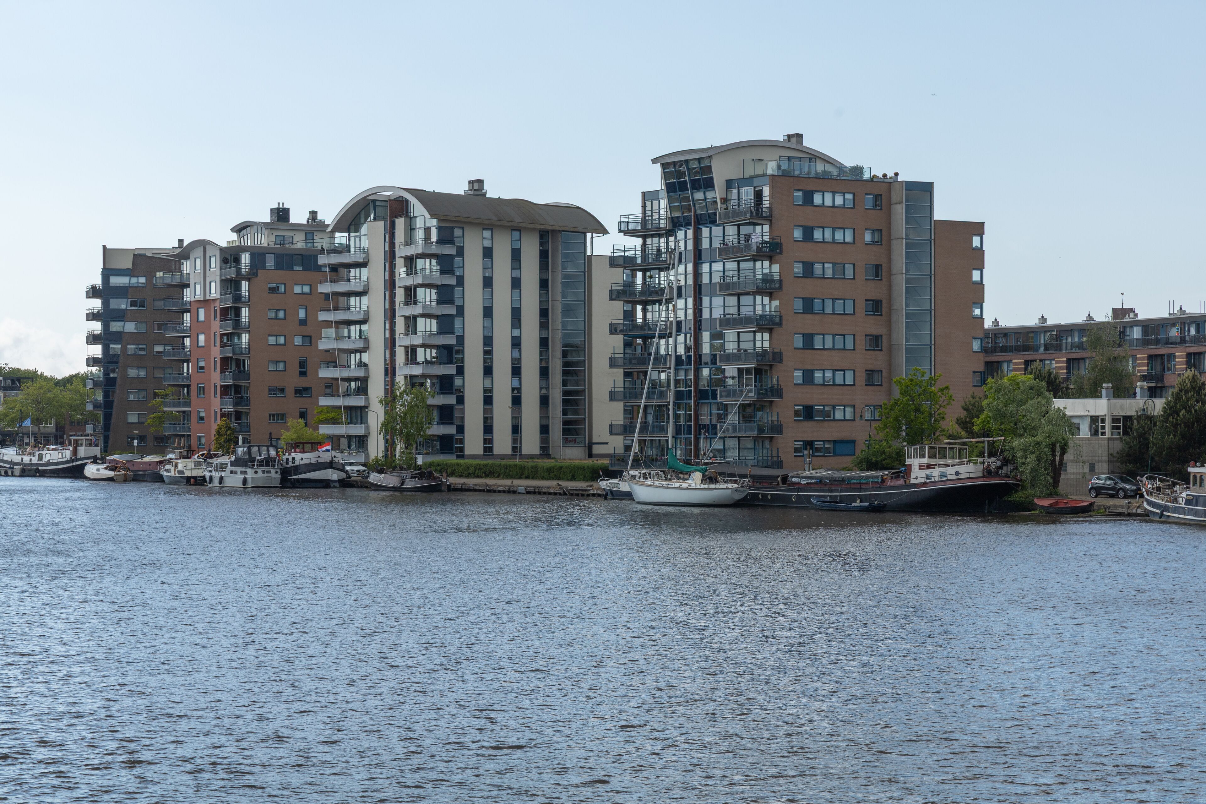 This contemporary waterside scene in Wormerveer, Netherlands, showcases modern residential buildings with unique architecture and boats docked along the calm water, under a bright sky.