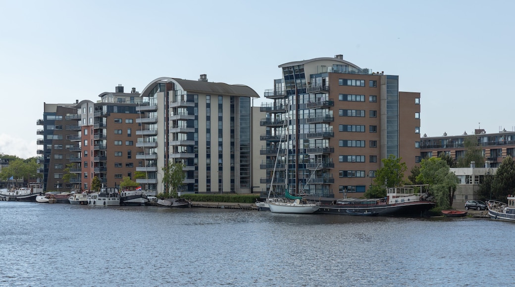 This contemporary waterside scene in Wormerveer, Netherlands, showcases modern residential buildings with unique architecture and boats docked along the calm water, under a bright sky.