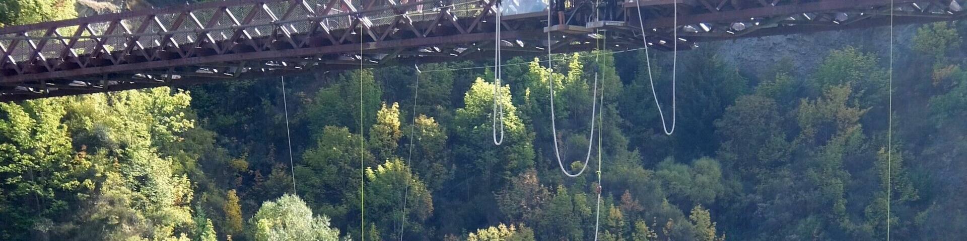 A bungee jumping platform with a bridge, a river, and a forested cliff.