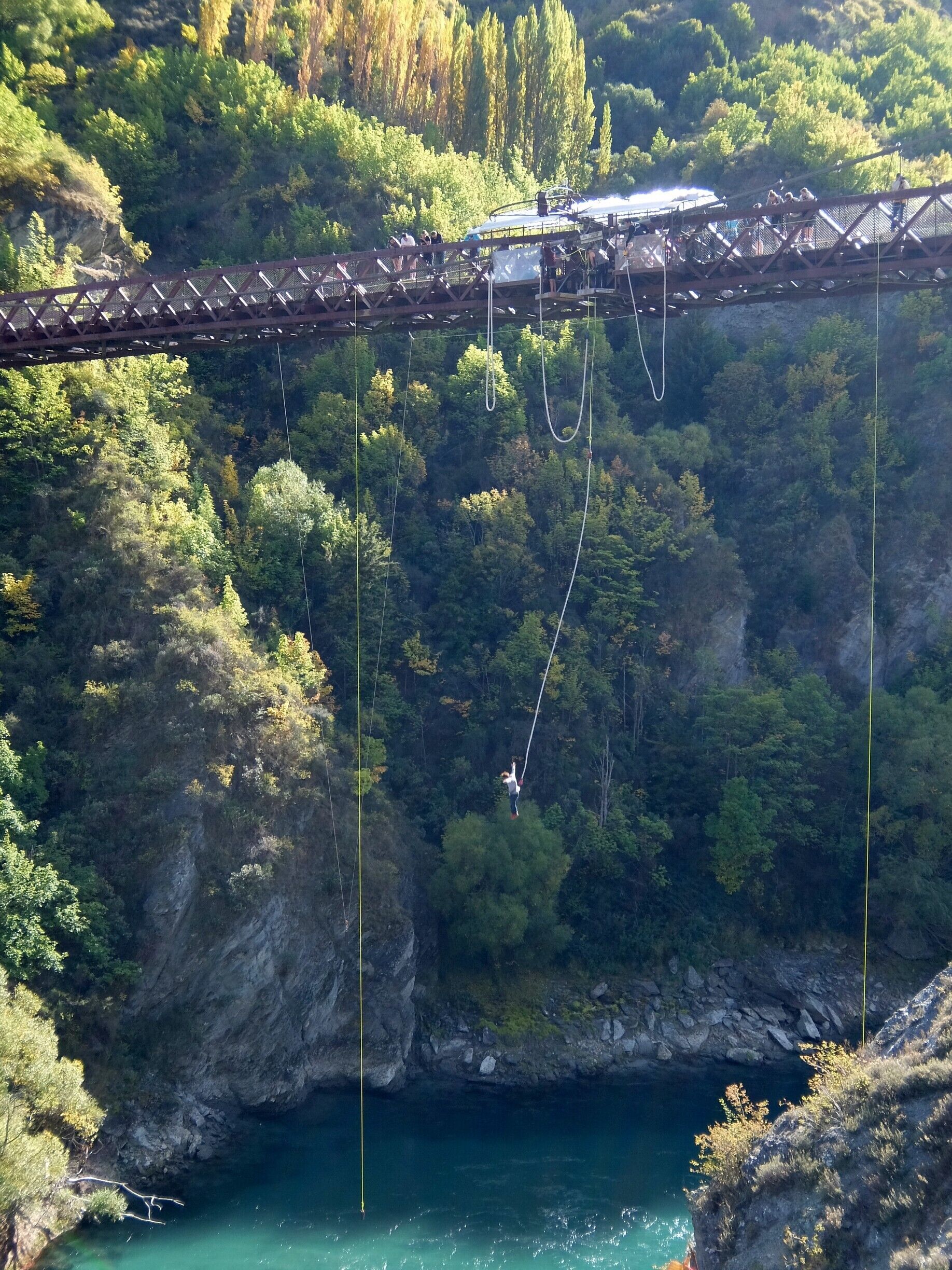 A bungee jumping platform with a bridge, a river, and a forested cliff.