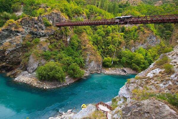 Un pont de chemin de fer enjambant une rivière, entouré d’une végétation luxuriante et d’un paysage rocheux.