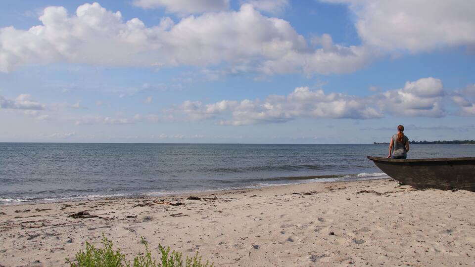 A beach with a woman in a boat, a clear sky, and distant land.