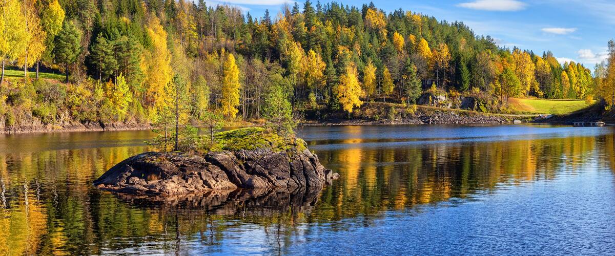 Panorama landscape of gold colorful fall time by the lake Tokke in Telemark region. Blue sky with white clouds . Nice reflections of little stone island in lake water. Autumn in Norway.
