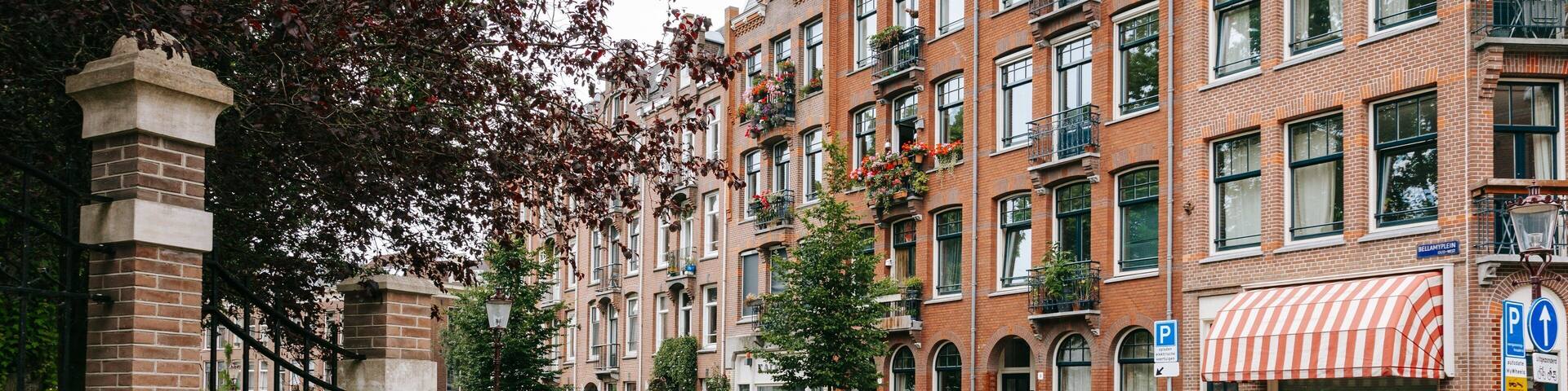 A street with red brick buildings, parked cars, and a cyclist.