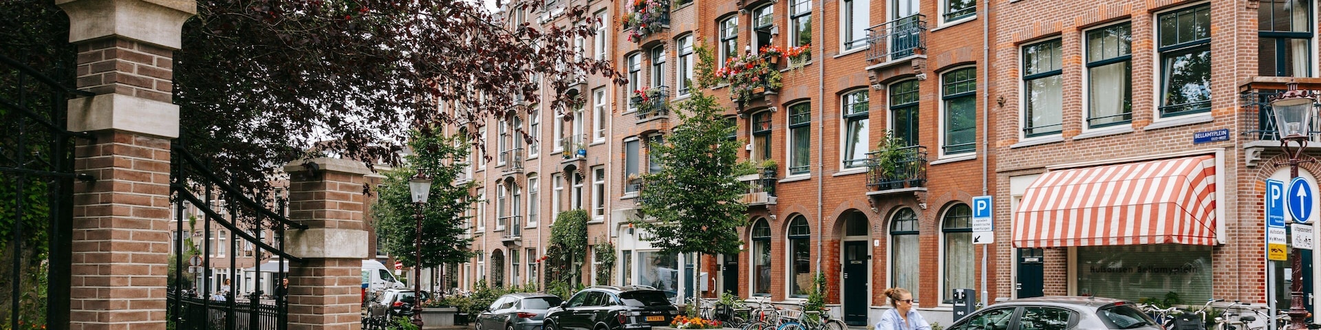 Rua com edifícios de tijolos vermelhos, carros estacionados e um ciclista.