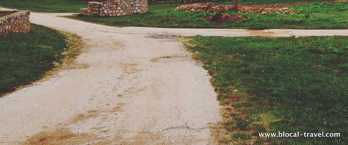A rural road with houses, a stone wall, and autumn-colored trees in the background.