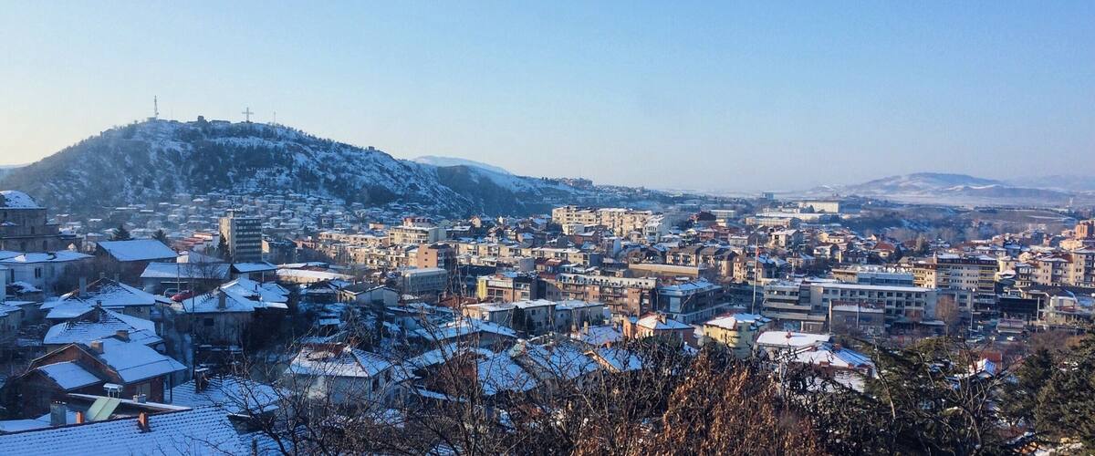 A snow-covered cityscape with buildings and a hill in the background.
