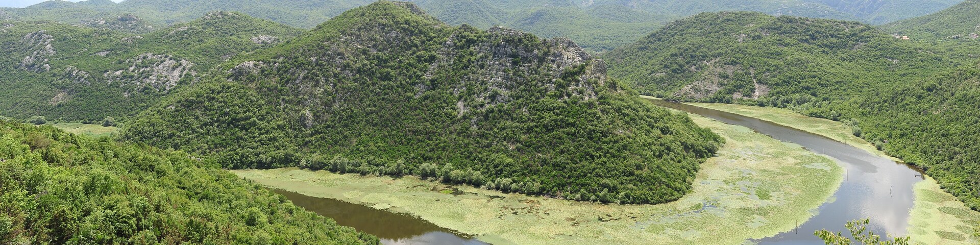 Un río serpentea a través de un valle exuberante y verde, con colinas boscosas al fondo.