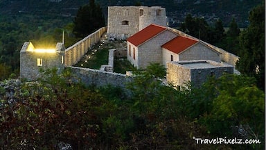 A stone fortress with a red roof surrounded by mountains.