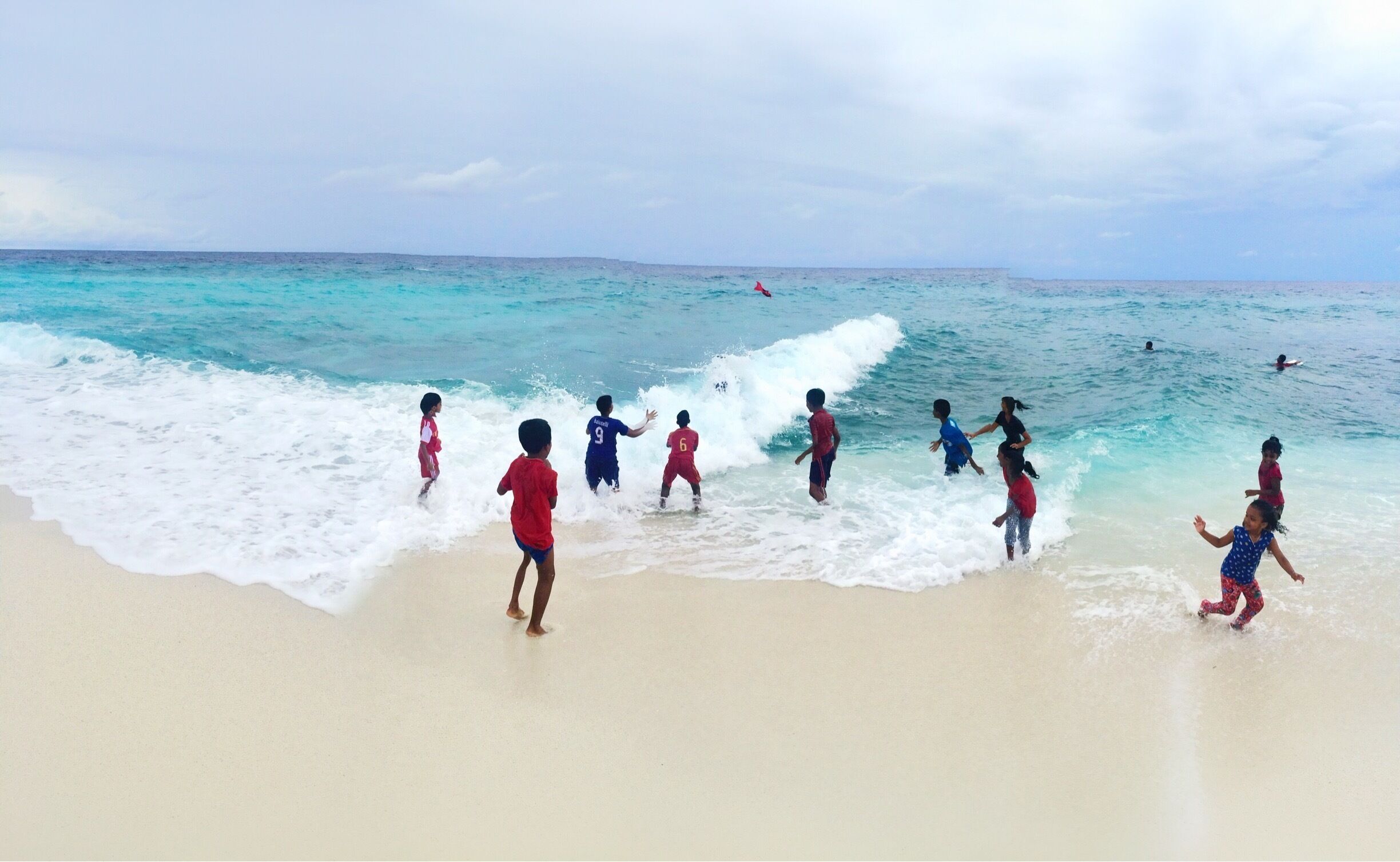 Crianças brincando em uma praia arenosa com ondas quebrando na costa.