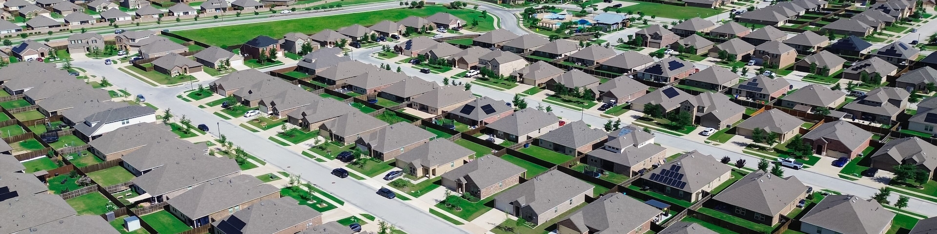 Uma área residencial com casas, ruas e um grande tanque d'água ao longe.