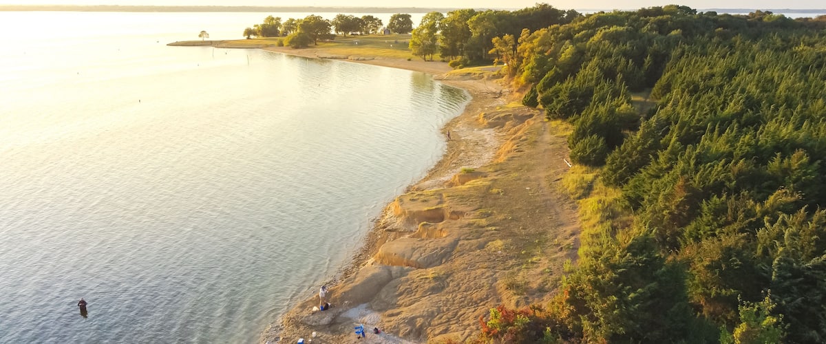 A lakeside view with a rocky shoreline, trees, and a distant shoreline.