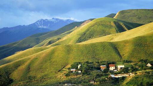 Rolling hills with a village at the base and snow-capped mountains in the background.