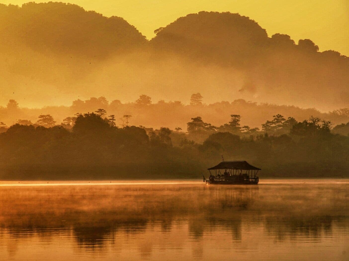 A boat on a calm lake with misty hills in the background.