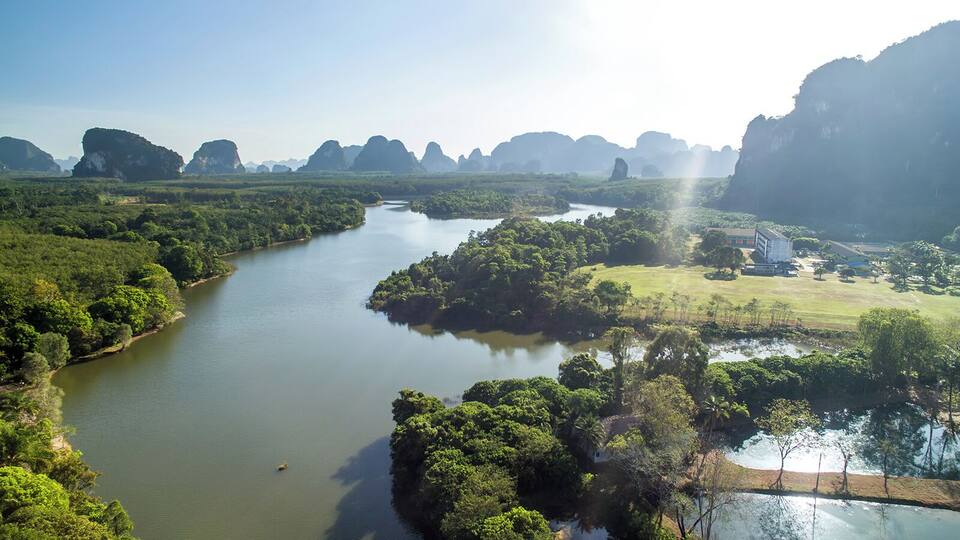 A river winding through a lush landscape with dense greenery and distant rock formations.