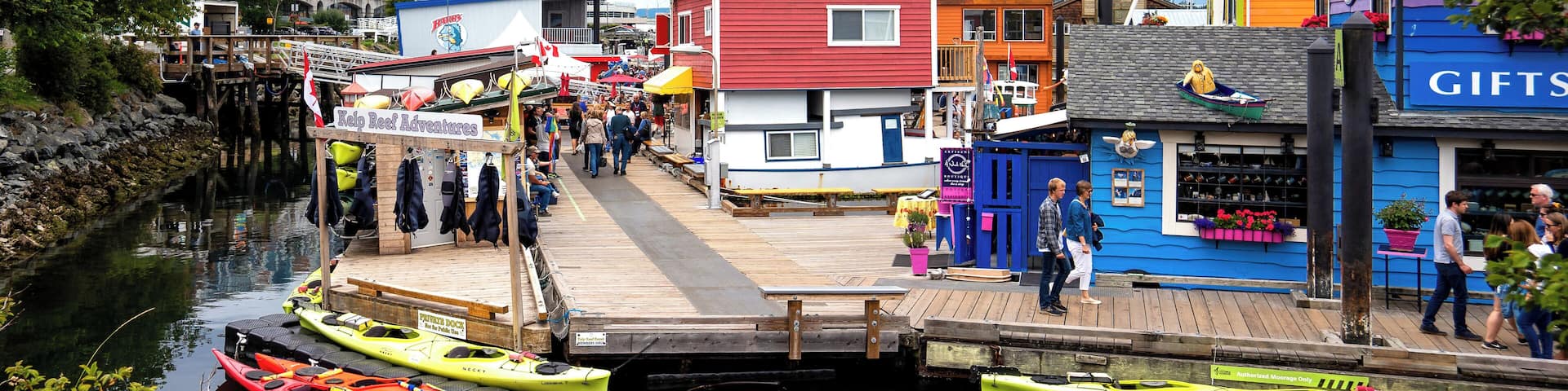 A waterfront with colorful buildings, a dock, and kayaks.